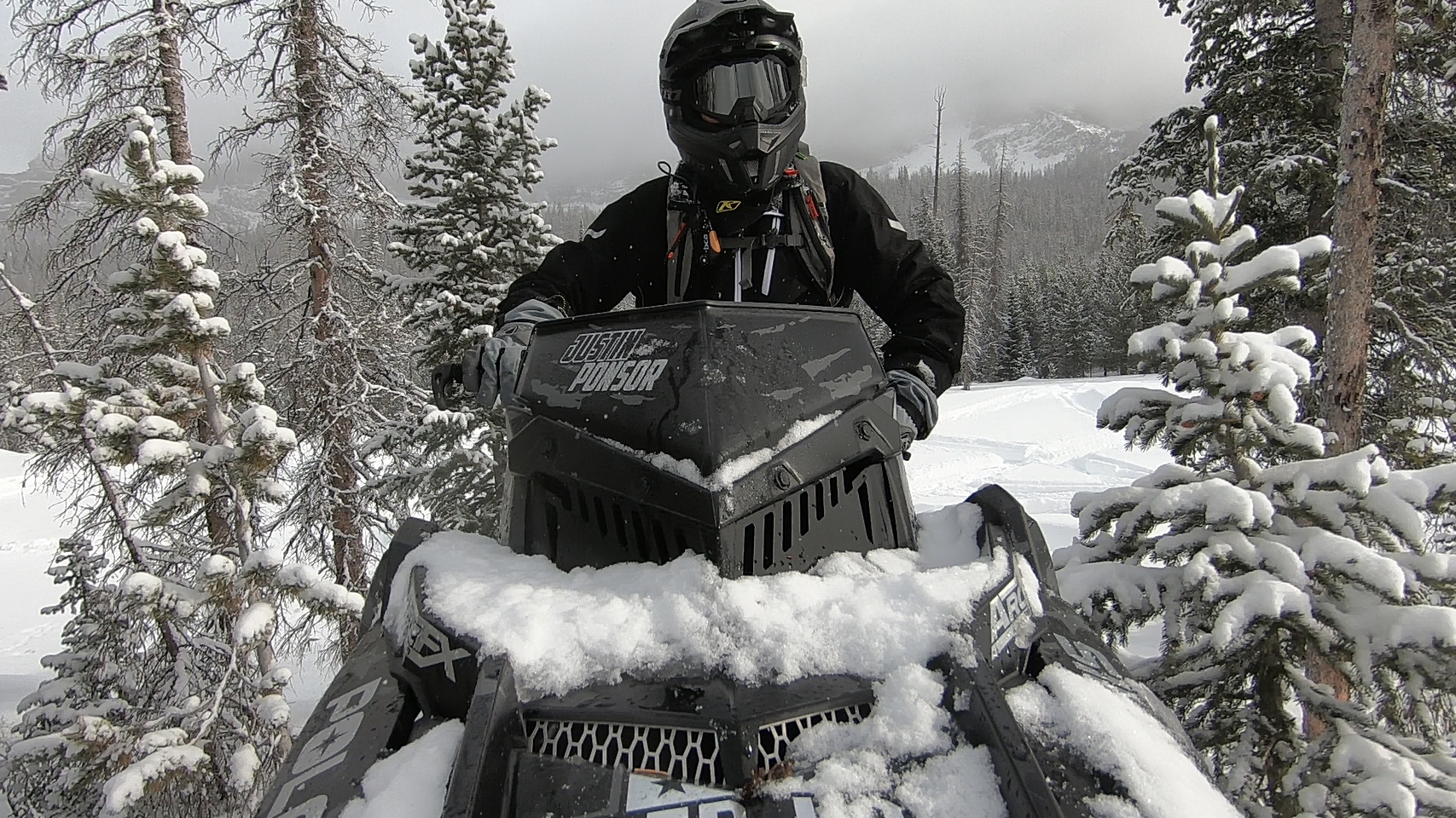 Justin Ponsor sitting on his snowmobile with a custom logo added to the windshield