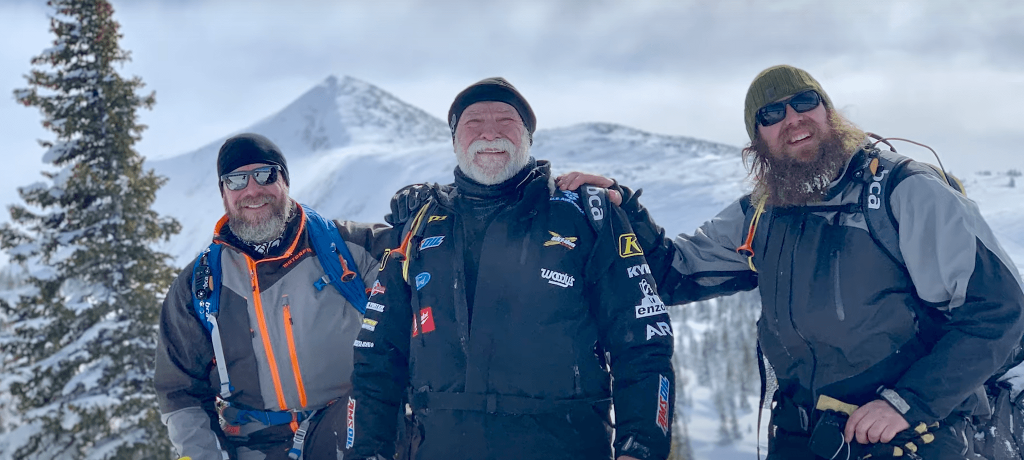 Three snowmobilers posing for a photo at the summit of a mountain