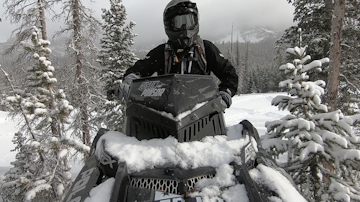 Justin Ponsor sitting on his snowmobile with a custom logo added to the windshield