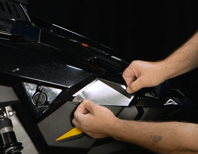 An easy-install vinyl wrap piece being applied to a Polaris Axys snowmobile